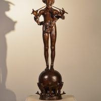Alt text: Bronze fountain sculpture of the deity Pan mischeviously playing two flutes, standing atop a sphere flanked by fish, frontal view