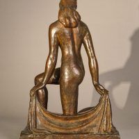 Alt text: Bronze sculpture of a nude dancer kneeling with one leg on the ground, holding a shawl behind her, rear view