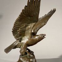 Alt text: Bronze sculpture of eagle preparing to take flight off a rocky point, angled view 