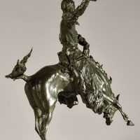 Alt text: Bronze sculpture of a rearing bronco with a cowboy on his back, holding his hat off his head with his right hand