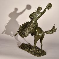 Alt text: Bronze sculpture of a rearing bronco with a cowboy on his back, holding his hat off his head with his right hand