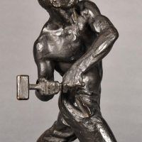 Alt text: Bronze sculpture of a muscular shirtless man swinging a hammer, detail