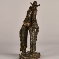 Alt text: Bronze sculpture of a standing cowboy with lasso, rear view
