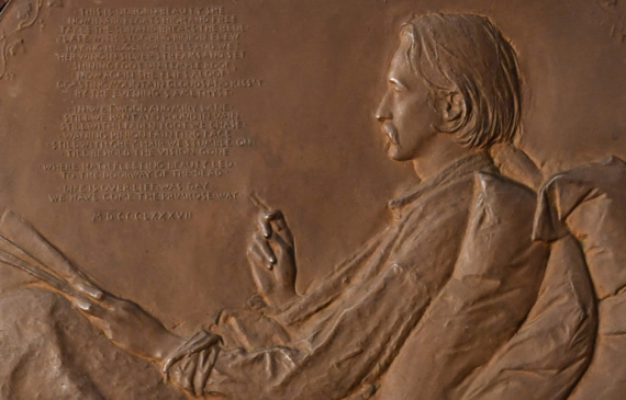 Alt text: Bronze bas relief of Robert Louis Stevenson writing in bed