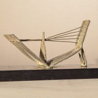 Alt text: Abstract soldered lead sculpture atop a wooden base resembling a drawbridge, angled view