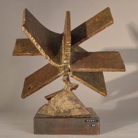 Alt text: Welded steel sculpture with many panels or blades, resembling a fan, rear view
