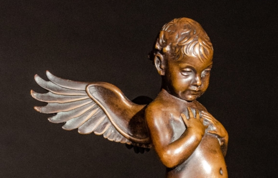 Alt text: Small bronze cherub sculpture with outstretched wings, angled view