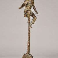 Alt text: Bronze sculpture of a circus performer riding a tall unicycle, angled view