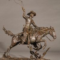 Alt text: Bronze sculpture of a cowboy with a lasso riding a horse jumping over a cactus, side view