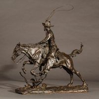 Alt text: Bronze sculpture of a cowboy with a lasso riding a horse jumping over a cactus, angled view