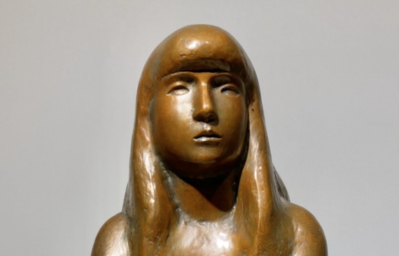 Alt text: Bronze sculpture of a girl with crossed arms, frontal view