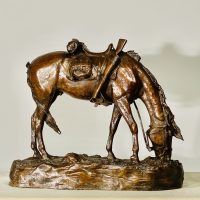 Alt text: Bronze sculpture of a saddled horse bending down to graze, side view