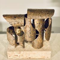 Alt text: Abstract bronze and steel assemblage mounted on a stone block, downward view