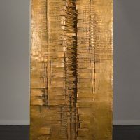 Alt text: Wide, vertical bronze column with concave center and abstracted incised pattern, rear view