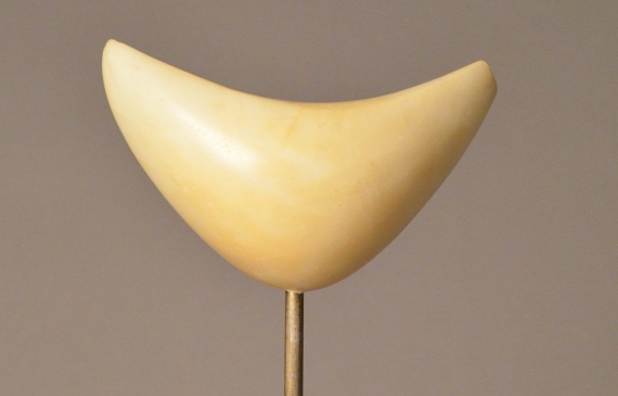 Alt text: Boomerang-shaped marble sculpture mounted on marble, attached by a short metal poll