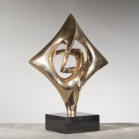 Alt text: Abstract diamond-shaped sculpture in bronze with points in each cardinal direction mounted on base, side view