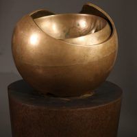 Alt text: Abstract bronze sphere atop a bronze column, frontal view