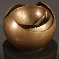 Alt text: Abstract bronze sphere atop a bronze column, angled view