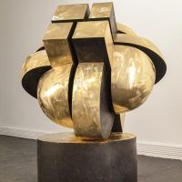 Alt text: Abstracted bronze sculpture that looks interlocking parts on a round base, side view