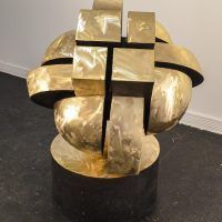 Alt text: Abstracted bronze sculpture that looks interlocking parts on a round base