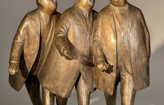 Alt text: Bronze sculpture of three businessmen in trench coats walking together, frontal view