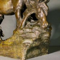 Alt text: Bronze sculpture of a horse bending down alongside a girl sitting near to the ground, peering over a cliff (detail)