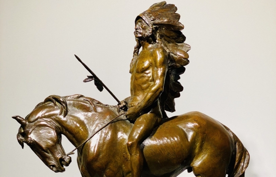 Alt text: Bronze sculpture of a Native American chieftain wearing an ornate headdress and riding on a horse