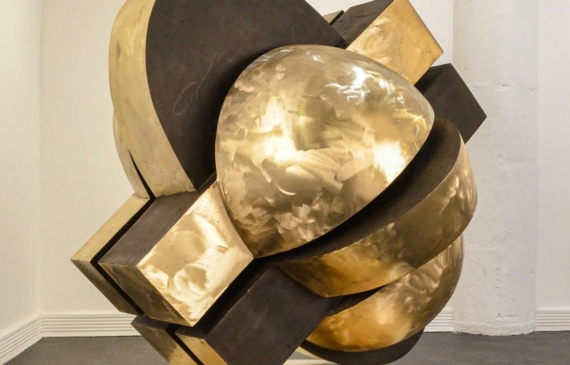 Alt text: Abstracted bronze sculpture that looks interlocking parts on a round base, side view