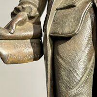 Alt text: Bronze sculpture of man holding a scroll, detail