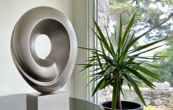 Alt text: silver, oval shaped sculpture next to a plant